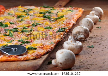 Long pizza with chicken and pineapple lies on a wooden table. Roman pizza on a wooden spatula. One meter long pizza. Pizza closeup  Royalty-Free Stock Photo #1935101237