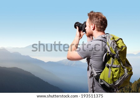 Young man with backpack taking a photo on the top of mountains, caucasian