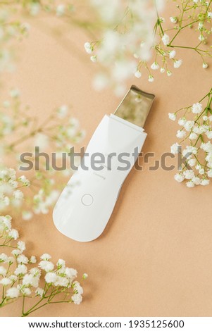 Ultrasonic Skin Scrubber Exfoliating Wand on tan background with babies breath flowers
