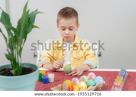 Preschooler boy focused on drawing an Easter pattern while sitting at the table in the kitchen. Easter family holiday celebration at home and craft concept.