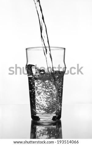 wine glass with water pouring on glass table (gray scale)