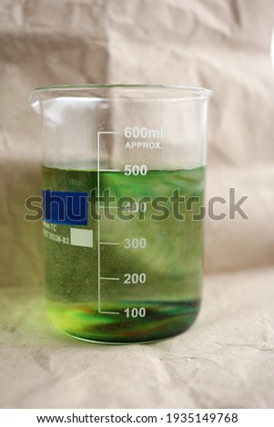In a large beaker, the green dye slowly dissolves in the water.