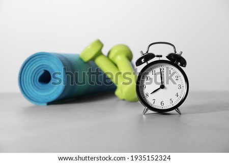Alarm clock, yoga mat and dumbbells on grey background. Morning exercise Royalty-Free Stock Photo #1935152324