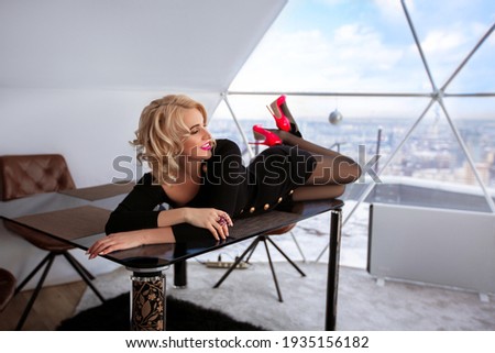 The girl secretary lies on the table in the office near the panoramic windows overlooking the city in a black dress
