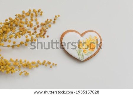  gingerbread cookie in a shape of a heart and mimosa flowers on white background. top view copy space