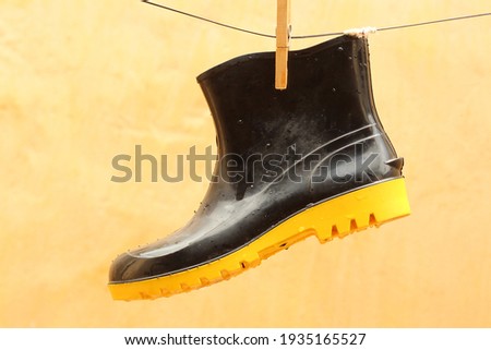 Black rubber boot, with yellow sole, hanging from the clothesline by a fastener, with a light background.