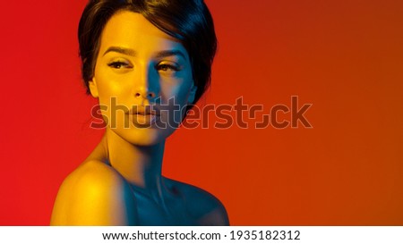 High fashion model metal red lips and face woman in colorful bright neon UV blue and yellow lights, posing in studio, beautiful girl, glowing makeup, colorful makeup. Glitter Bright Neon Makeup