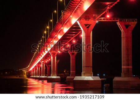 Side view of colourful bridge illuminated with red color lights at the night. Bridge stands on Volga river in Russia. Red light is reflected in the water.