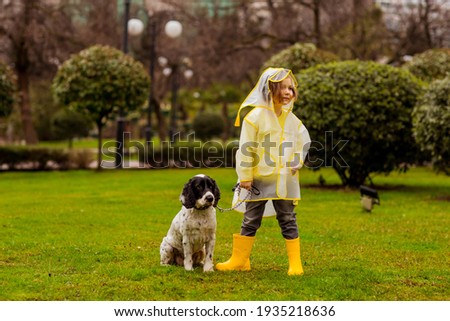 a beautiful girl in a yellow raincoat with a hood,and yellow boots, walks in the park with her favorite dog of the Russian Spaniel breed, on a spring day