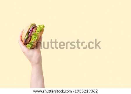 Female hand with tasty burger on yellow background, close up.