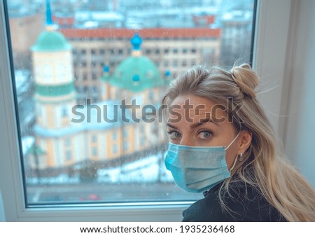 
photo of a girl sitting on a windowsill wearing a masklooking towards the camera