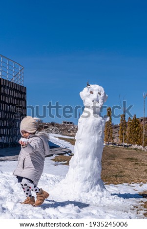 A sweet baby girl playing with a snowman