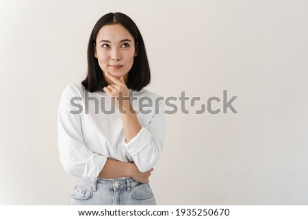 Beautiful brunette woman over isolated background with hand on chin thinking about question, pensive expression. Girl with thoughtful face. Doubt concept. Royalty-Free Stock Photo #1935250670