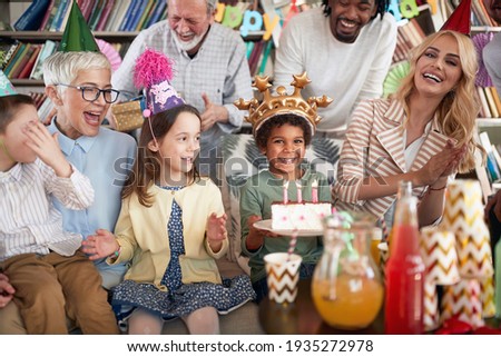 A happy little boy posing for a photo holding a cake at his birthday party in a festive atmosphere at home with family and friends. Family, celebration, together