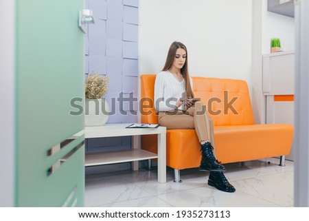 young woman in the waiting room interview sitting on sofa in corridor of dentist office or reception modern medical center while doctor's appointment. using mobile phone fills information or resumes Royalty-Free Stock Photo #1935273113