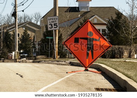Bright orange and black flagger or flagman sign on the side of the road