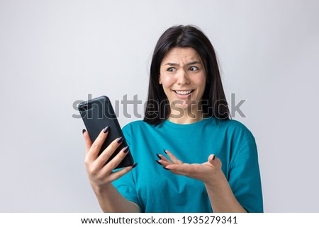 Front portrait of young smiling woman using mobile phone against grey background