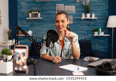 Famous blogger recording red lipstick review for beauty vlog. Woman vlogger making live make up tutorial share on social media using professional microphone looking at camera for digital podcast