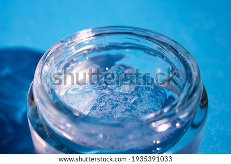 Jar with a transparent cosmetic product, gel or cream on a blue background. Antioxidant self-care cream. Side view.