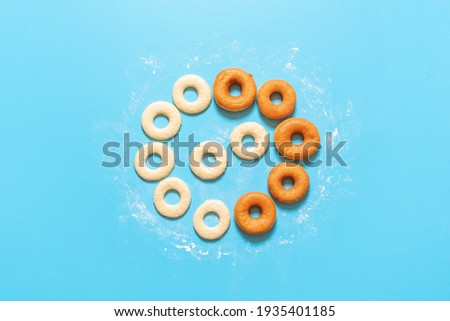 Making donuts recipe. Uncooked yeast-raised dough in circle shape and fried doughnuts, on a blue background. Flat lay with homemade ring donuts. Royalty-Free Stock Photo #1935401185