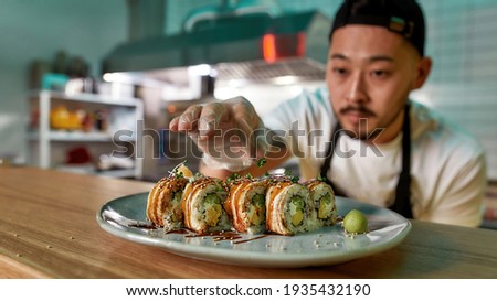 Professional sushi chef wearing protective gloves decorating rolls served on plate at commercial kitchen. Food photography, Asian cuisine, restaurant service concept