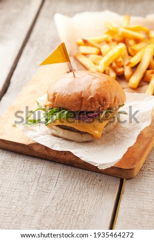 Tasty home made burger served with crispy fries. Rustic hamburger and potato chips composition with baking paper and wooden table. 