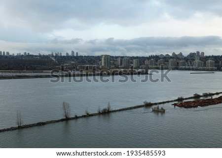 Container terminal in Vancouver, Canada in winter with a skyline of the city on the horizon. In the foreground there are logs macerated in water.
