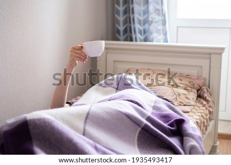 raised hand of person in bed holding a cup of tea early in the morning