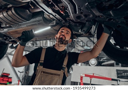 Professional auto mechanic working on the undercarriage of a car. Diligence, attention, inspection, examination, annual checkup, safety, insurance, professionalism, vehicle concept. Bottom view. Royalty-Free Stock Photo #1935499273