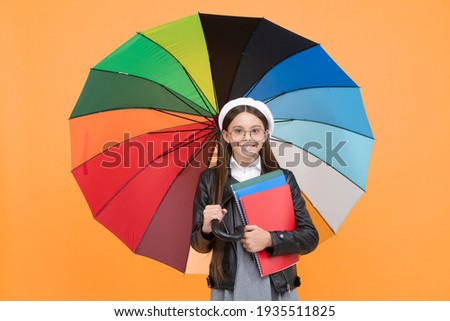 happy teen girl in glasses and beret under colorful umbrella for rain protection in autumn season hold notebook, fall season.