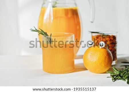 funny food concept. orange with eyes and orange and sea buckthorn juice for kids menu. rosemary leaves on a glass. healthy chidlren food and drinks.
