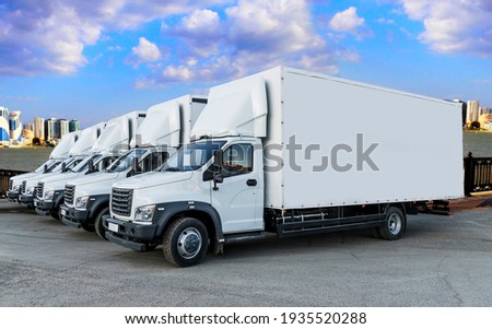 Some trucks are parked in a parking lot next to a logistics warehouse by the river. Several trucks are lined up in the parking lot. Logistic transport Royalty-Free Stock Photo #1935520288