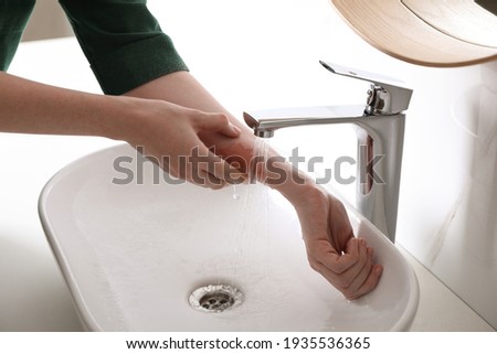 Woman putting burned hand under running cold water indoors, closeup Royalty-Free Stock Photo #1935536365