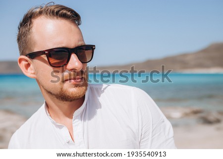 portrait of a young man in sunglasses and a white shirt against the background of the sea and rocks. Sumer holidays . High quality photo