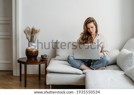 Portrait of a young happy female freelancer sitting on the couch and working on project, watching movie on laptop, studying, blogging, resting and chatting online. High quality photo Royalty-Free Stock Photo #1935550534