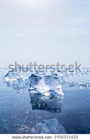 Beautiful shiny transparent pieces of blue ice on the mirror surface of the frozen Baikal Lake on a sunny frosty winter day. Natural cold background. Free space for text, blank. Close-up view, mock up