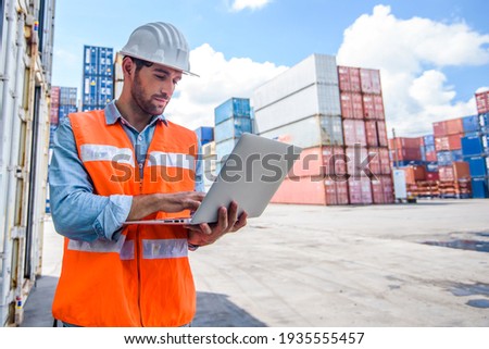 Confident man engineer wearing white safety helmet using computer laptop and check for control loading containers box from Cargo freight ship for import and export, transport Royalty-Free Stock Photo #1935555457