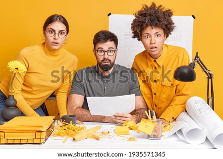 People teamwork and collaboration concept. Three shocked collaegues partners cooperate for creating architectural plan stare surprised at camera pose at office desk work on building project. Royalty-Free Stock Photo #1935571345