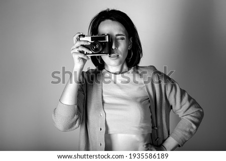A young girl in a sweater and a top poses with a vintage film camera on a light background. Black and white photo.