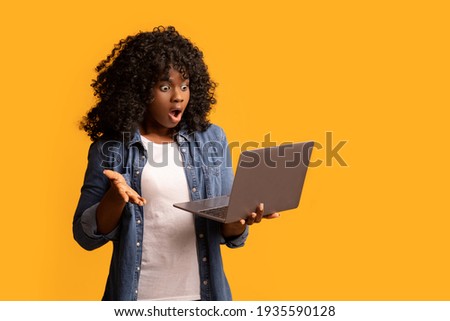 Shocked black lady using laptop, yellow background