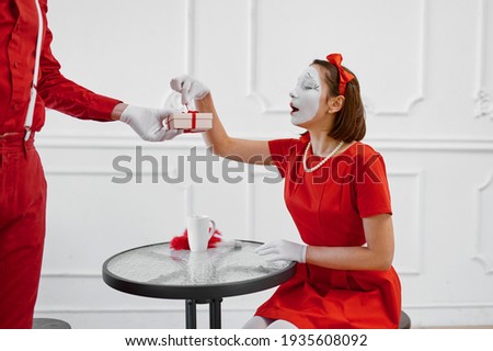 Two mime artists in red costumes, scene with gift