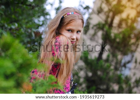 A young girl is resting in the school yard during a school break and preparing for the next lesson. Portrait of a young cute girl among the green trees