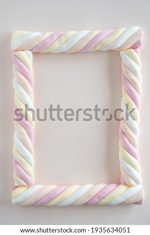 Top down view of marshmallow sweets (in Dutch: kabelspekjes) in the form of a picture frame on soft pink background, with copy space in the center