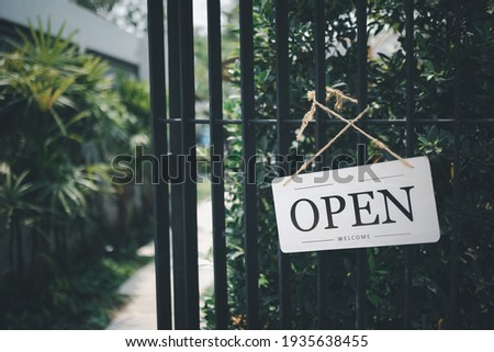 Open sign hanging in front of cafe gate with green garden background
