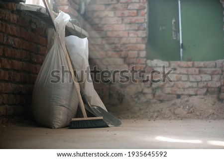 Shovel, broom and bags with a construction garbage on the dusty construction site floor background.