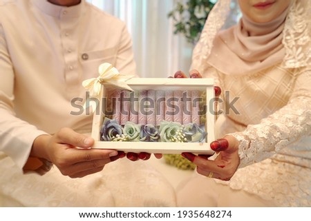 Malaysia Indonesia bride and groom holding together a set roll ringgit malaysian money inside a light wooden box, selective focus