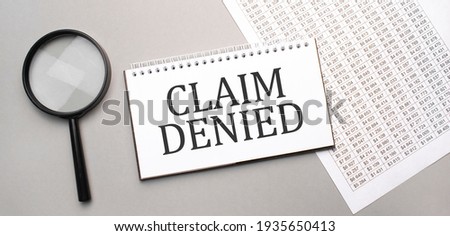 CLAIM DENIED sign in white paper notepad and magnifying glass on the grey background