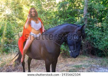 Young woman on horseback with sunlight, red cloak and fashionable bikini. Little red riding hood. High quality and high resolution photography.