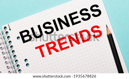 On a light blue background, a checkered notebook with the words BUSINESS TRENDS and a black pencil.