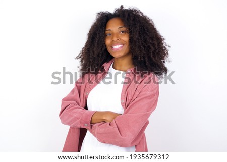 young beautiful African American woman wearing pink jacket against white wall happy face smiling with crossed arms looking at the camera. Positive person.